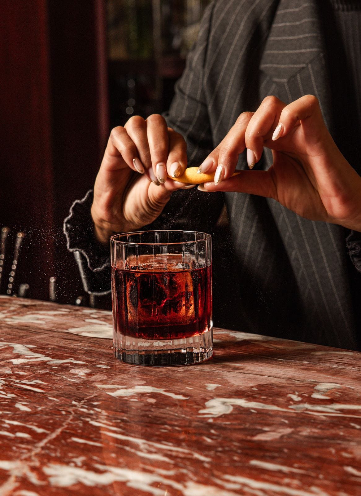 Zeste d'orange pressé au-dessus d'un Negroni, brume d'huiles essentielles visible dans la lumière